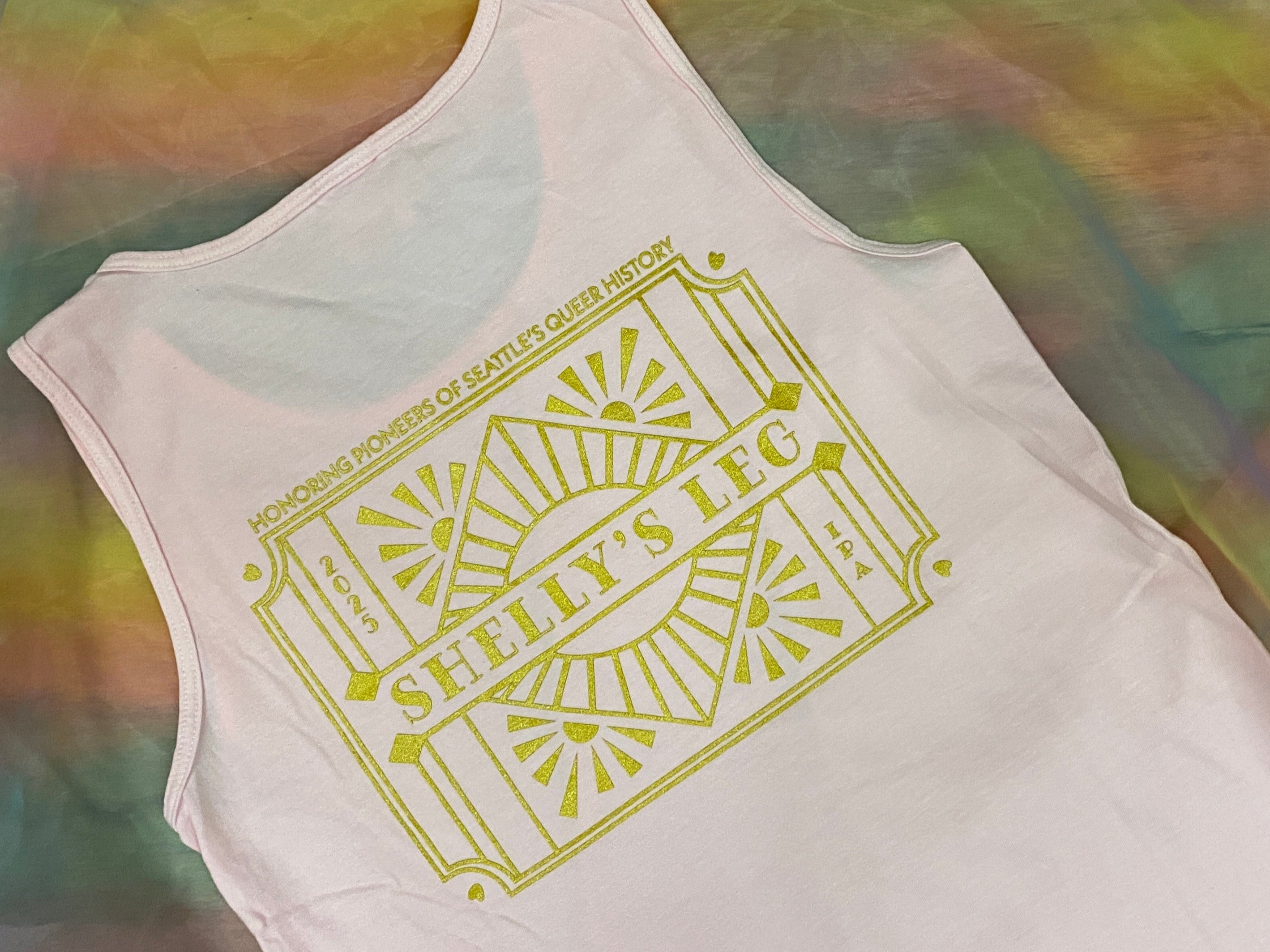 pale pink tank with an art deco style design that reads: honoring pioneers of seattle's queer history, shelly's leg IPA, 2025