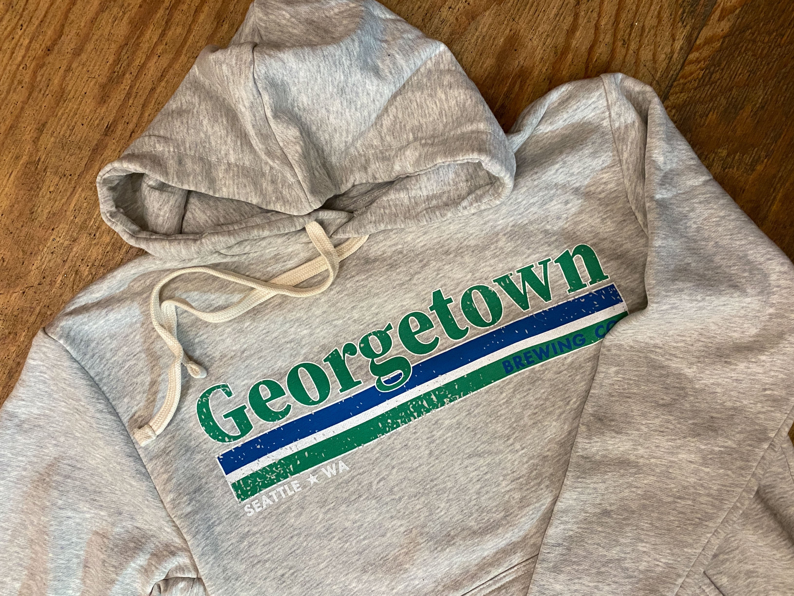 Offwhite heathered hoodie with 'Georgetown' printed on it in green and blue, on a wooden surface.