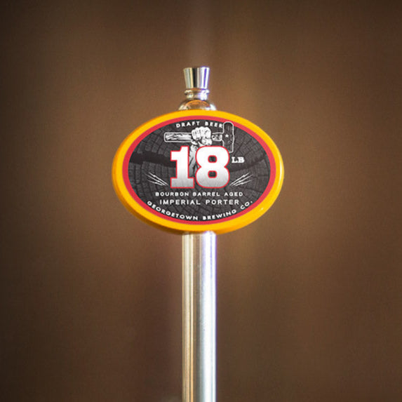 a yellow oval tap handle with a sticker for 18 pound barrel aged porter