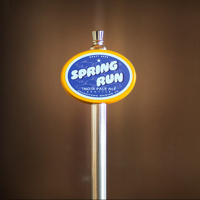 A close-up of a beer tap handle with a 'Spring Run' beer sign, predominantly yellow with a circular shape, mounted on a tap handle.