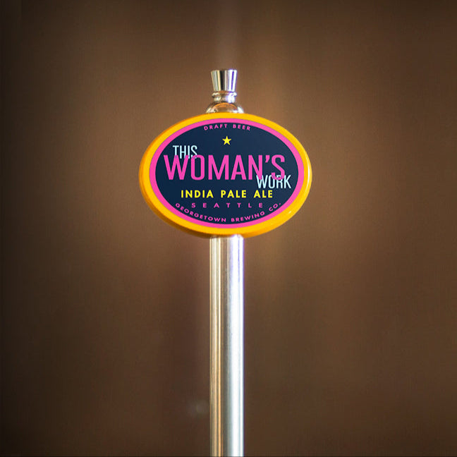 Beer tap handle with 'This Woman's Work' branding against a brown background