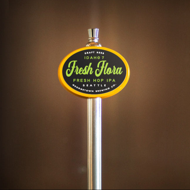 yellow oval beer tap handle with 'Fresh Flora' label on a brown background