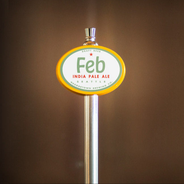 Beer tap handle with 'Feb' India Pale Ale label on a blurred brown background