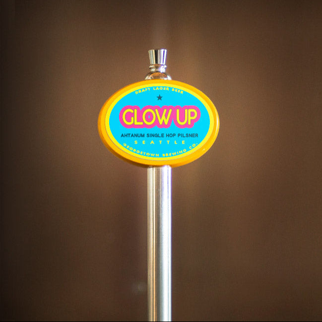 yellow oval beer tap handle with 'GLOW UP' sign on a brown background