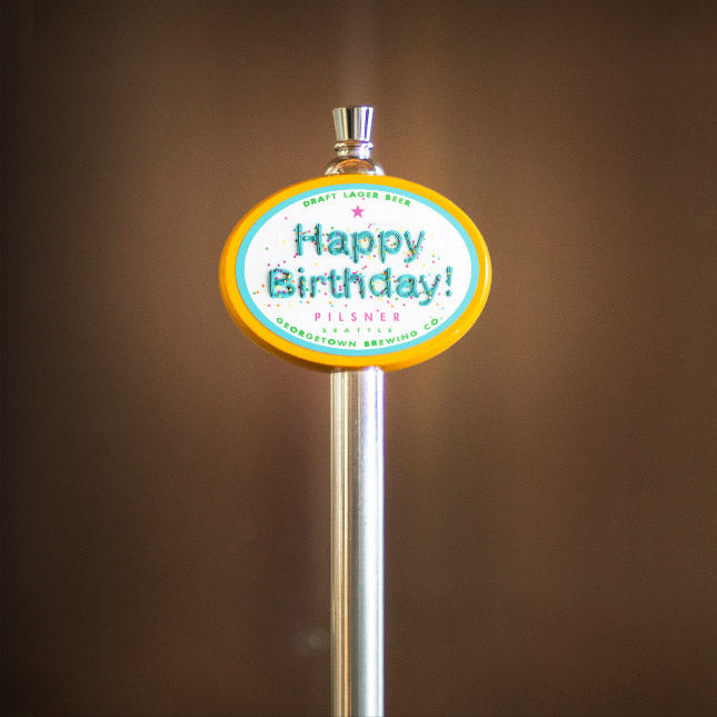 beer tap handle with a 'Happy Birthday!' sign on a blurred brown background