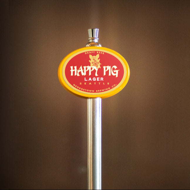 Happy Pig Lager tap handle on a blurred brown background