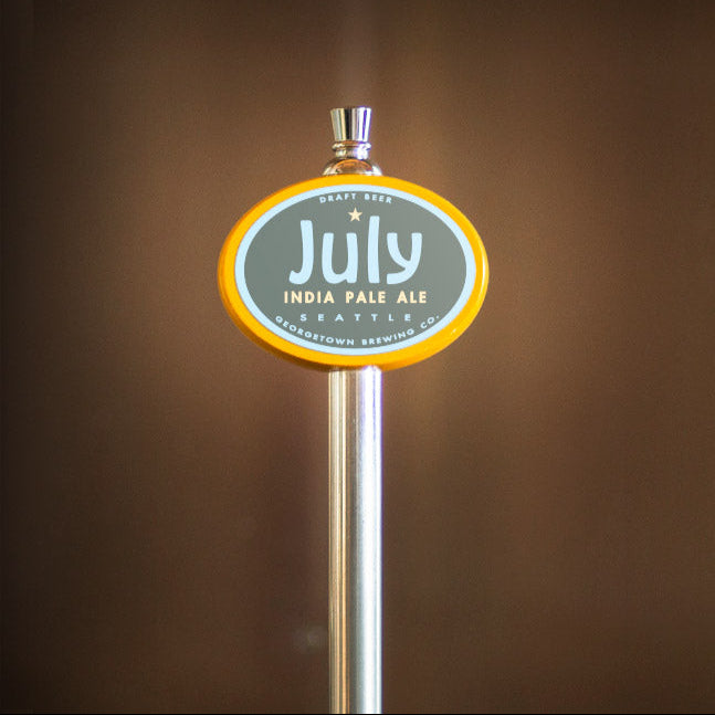 Tap handle with 'July' India Pale Ale label on a blurred brown background