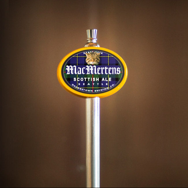 Metallic beer tap handle with 'MacMertens Scottish Ale' label against a brown background