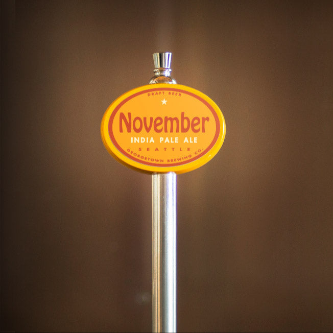 Beer tap handle with 'November India Pale Ale' label on a blurred brown background