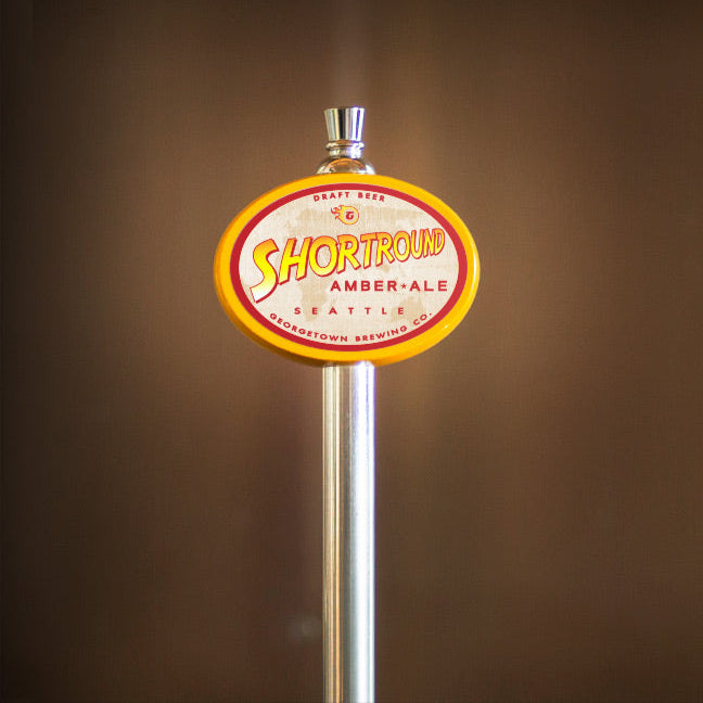 Beer tap handle with 'Shortround Amber Ale' label on a brown background