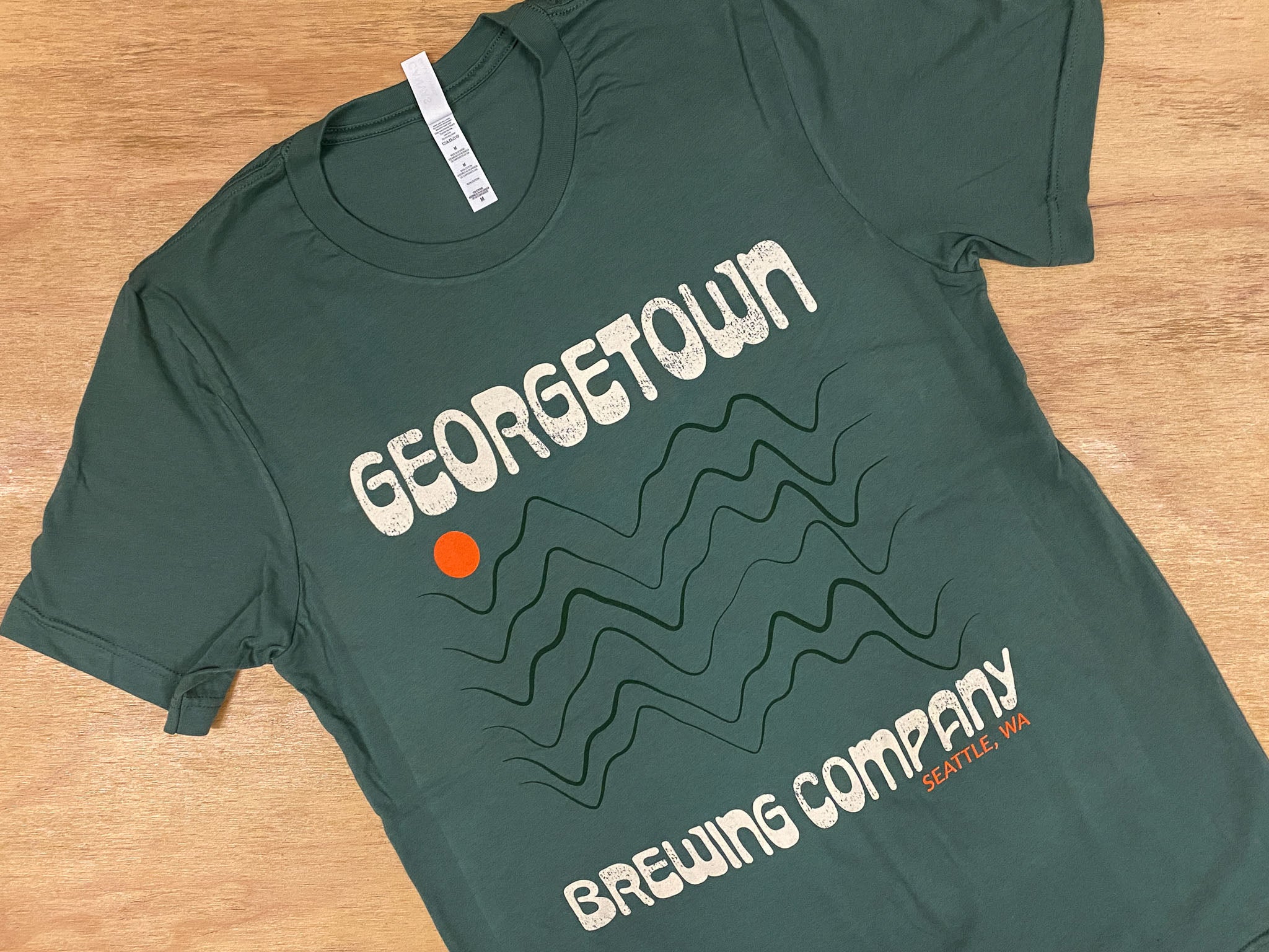 a green shirt that says Georgetown Brewing company in cream, with an orange sun and dark green wave design