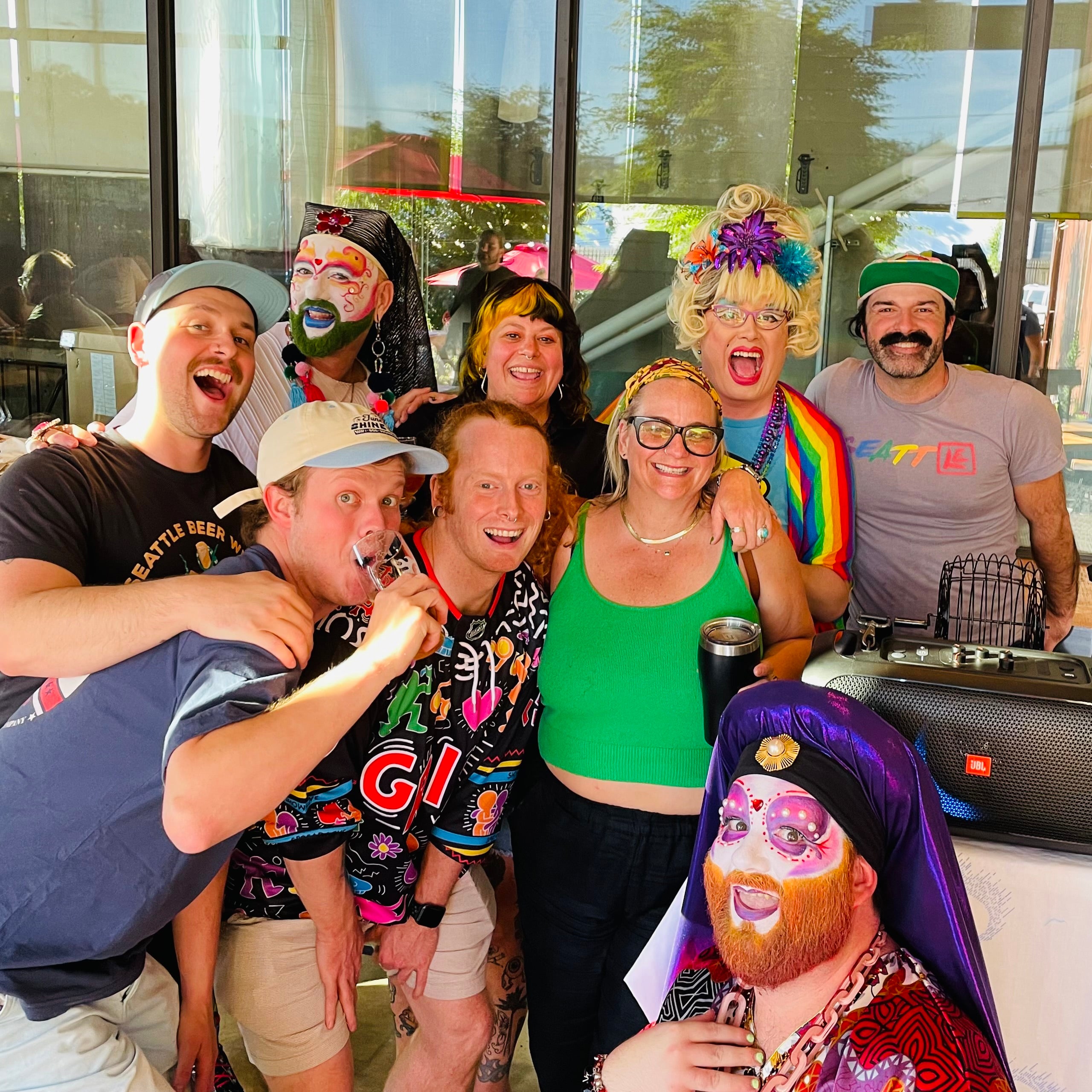 Group of people posing together with colorful costumes and props in front of a glass door.