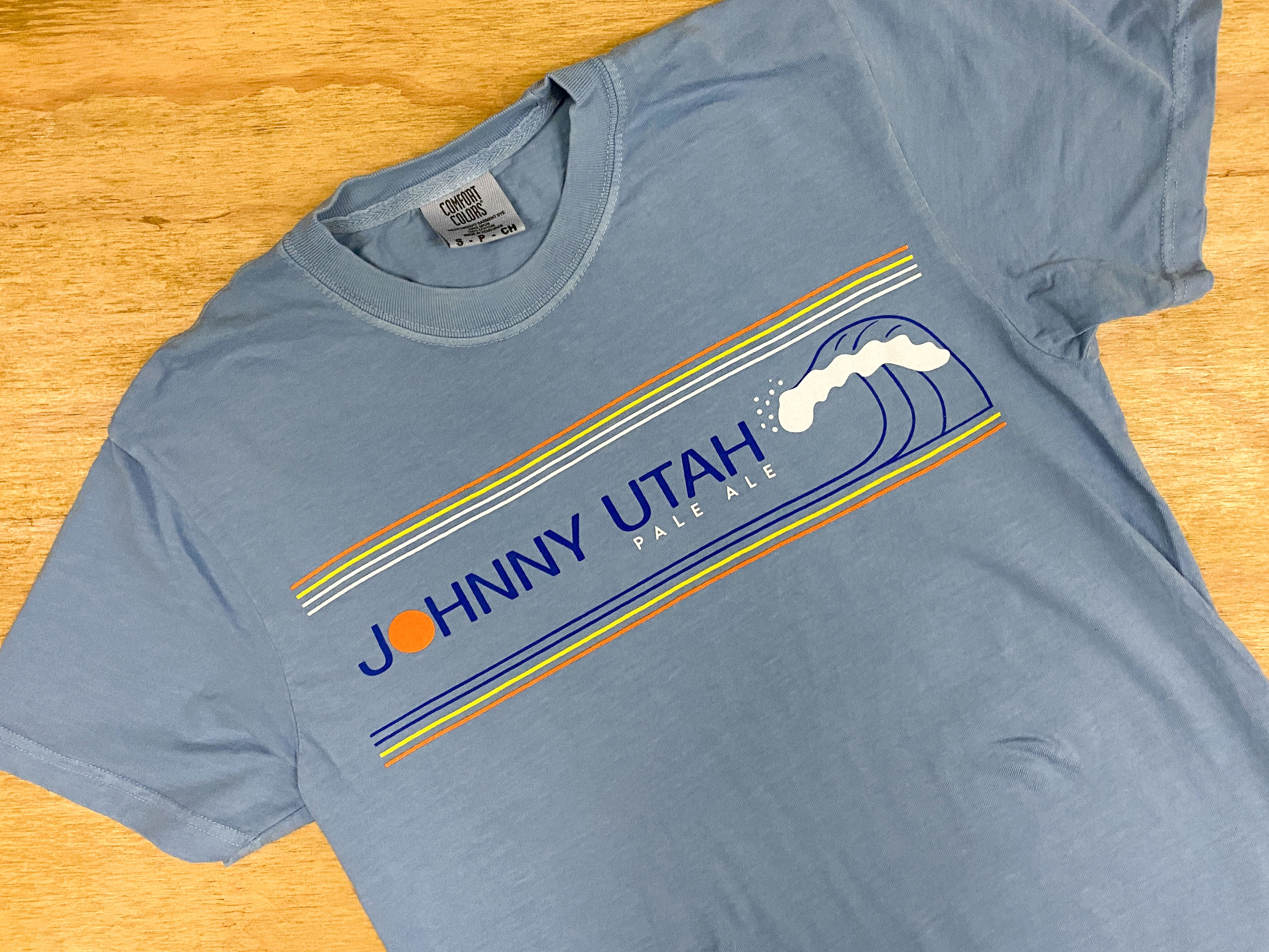 Blue t-shirt with 'Johnny Utah' graphic on a wooden surface