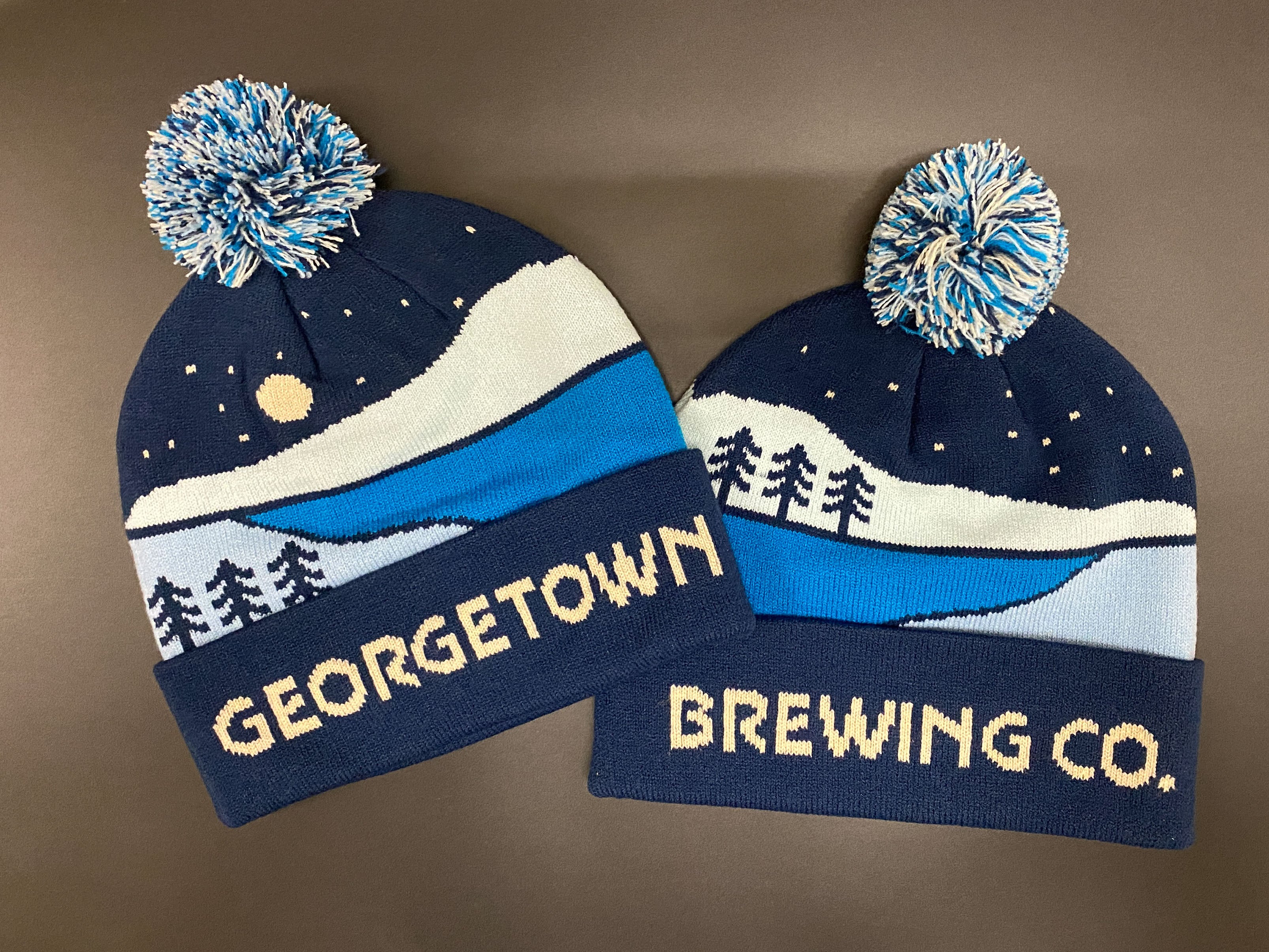 Two Georgetown Brewing Co. beanies with winter-themed designs in shades of blues. 