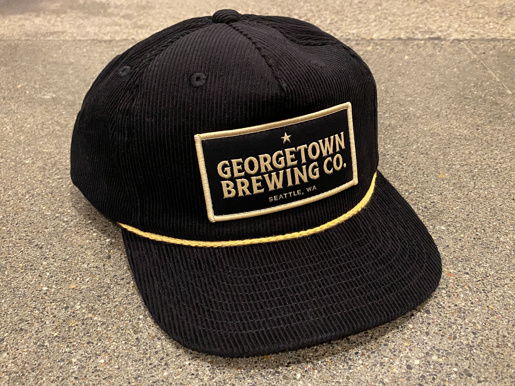 a black corduroy hat with a gold rope detail and patch that says Georgetown Brewing Co Seattle WA in gold and black