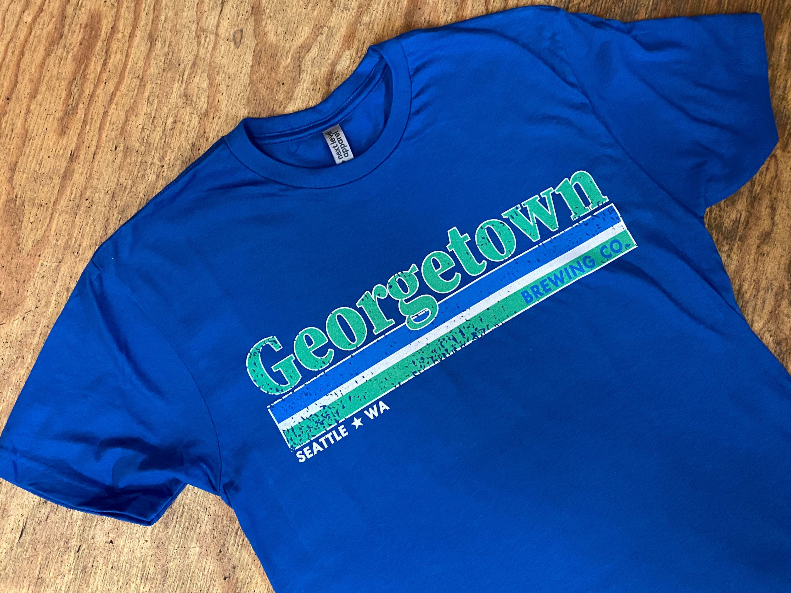Blue t-shirt with 'Georgetown' and 'Seattle, WA' text on a wooden surface