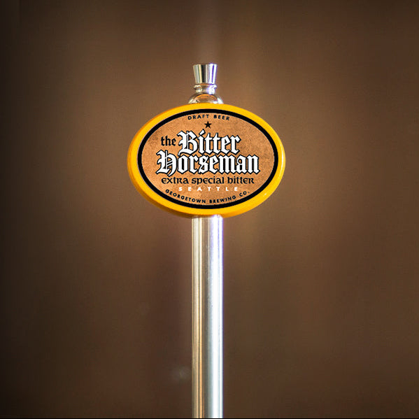 A close-up of a beer tap handle with an oval sign reading 'The Bitter Horseman' on a metallic pole against a dark brown blurred background.
