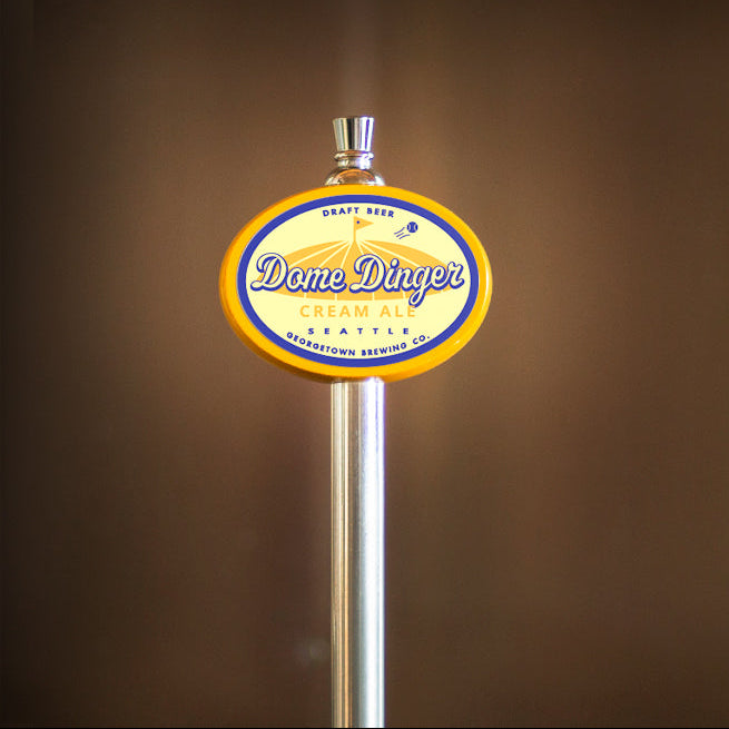 Dome Dinger Cream Ale logo on a metal tap handle against a brown background