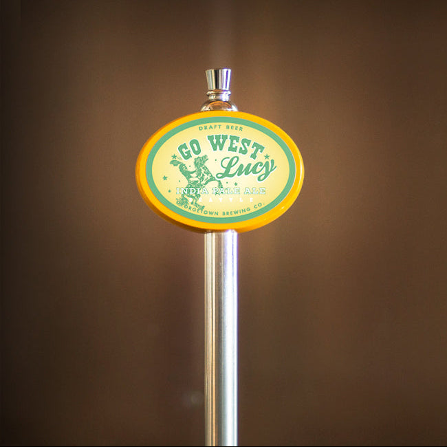 Metallic beer tap handle with 'Go West Lucy' label against a brown background