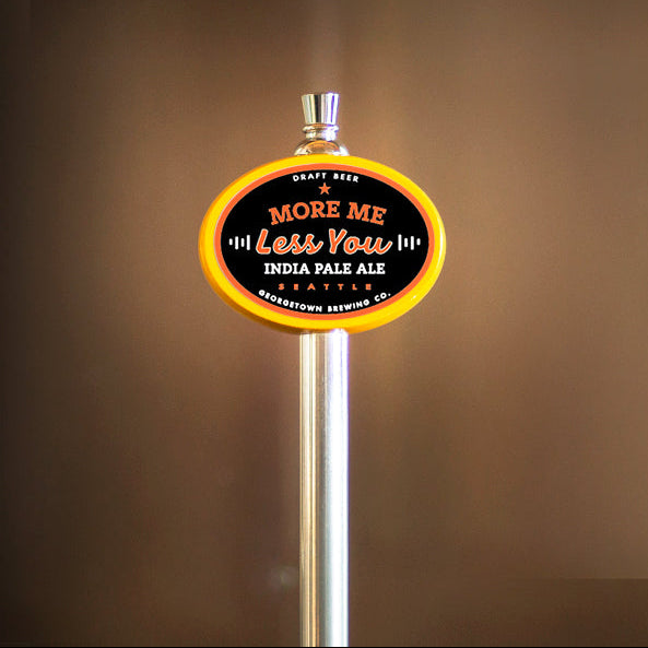 A beer tap handle for More Me Less You India Pale Ale by Republic Brewing Co., featuring a black oval sign with yellow lettering and a yellow outer rim, mounted on a silver metal post against a warm brown gradient background.