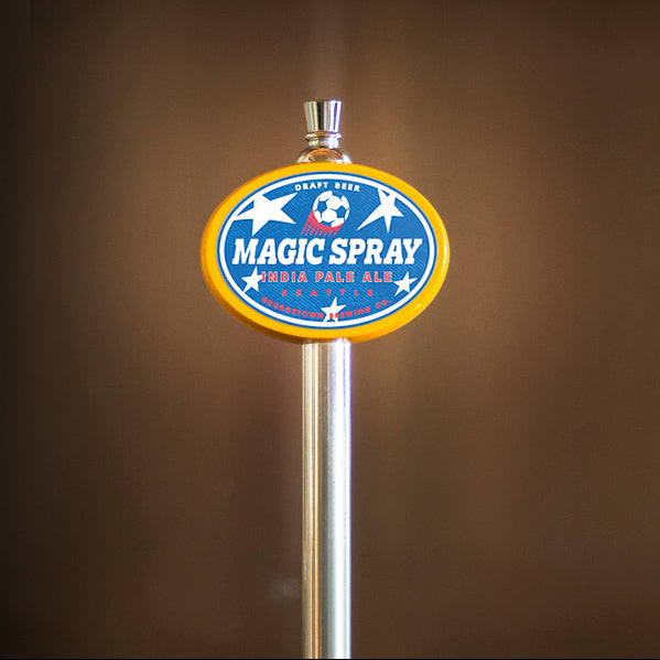 Metallic beer tap with 'Magic Spray' label against a brown background