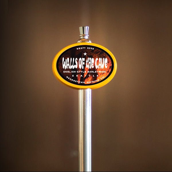 A close-up of a bar tap handle with an oval sign reading 'Walls of The Cave' on a dark brown blurred background.