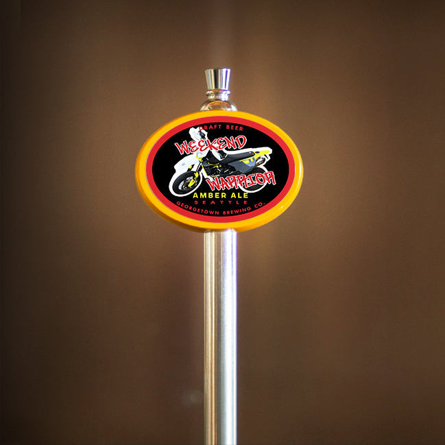 Beer tap handle with a colorful label reading Weekend Warrior and a photo of a motorcycle against a brown background