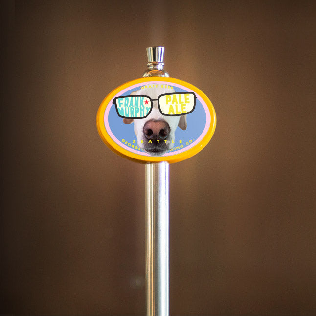 Metallic beer tap handle with a colorful label featuring a dog and text on a brown background