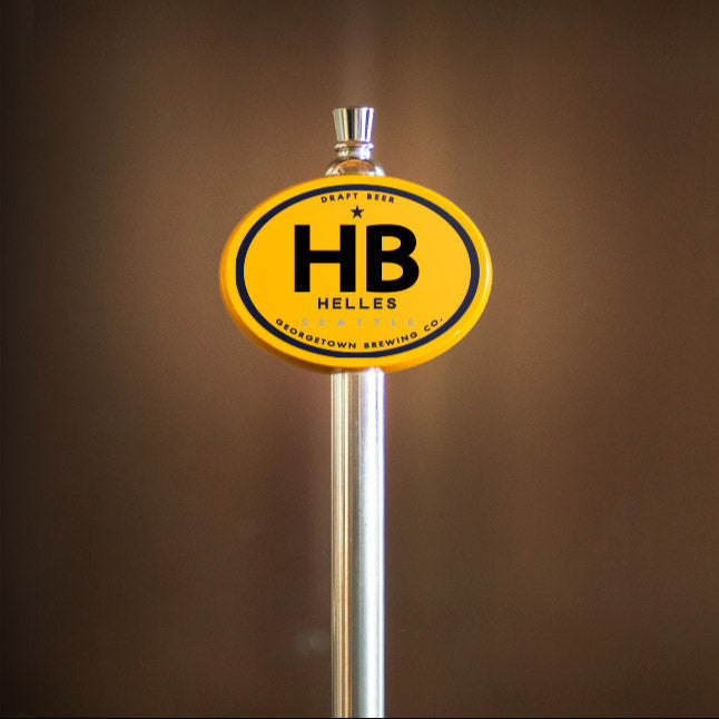 Yellow and black HB Helles beer tap handle on a brown background
