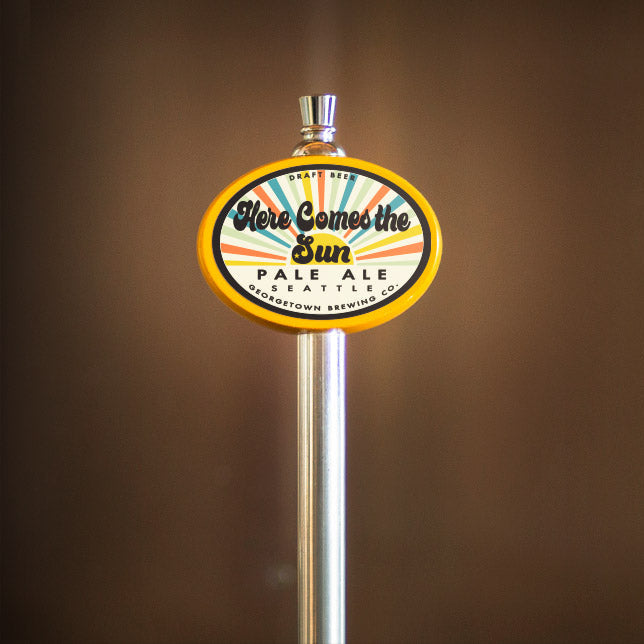 Beer tap handle with a Here Comes the Sun label against a brown background