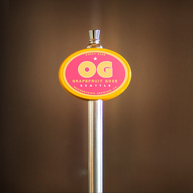 tap handle with a pink and yellow OG Gose label on a blurred brown background