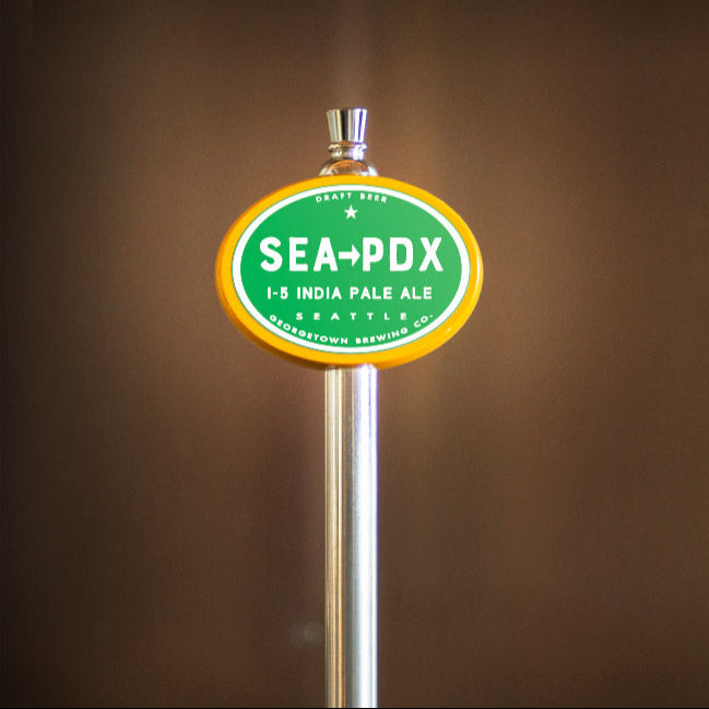 Beer tap handle with 'SEA-PDX' label on a blurred background