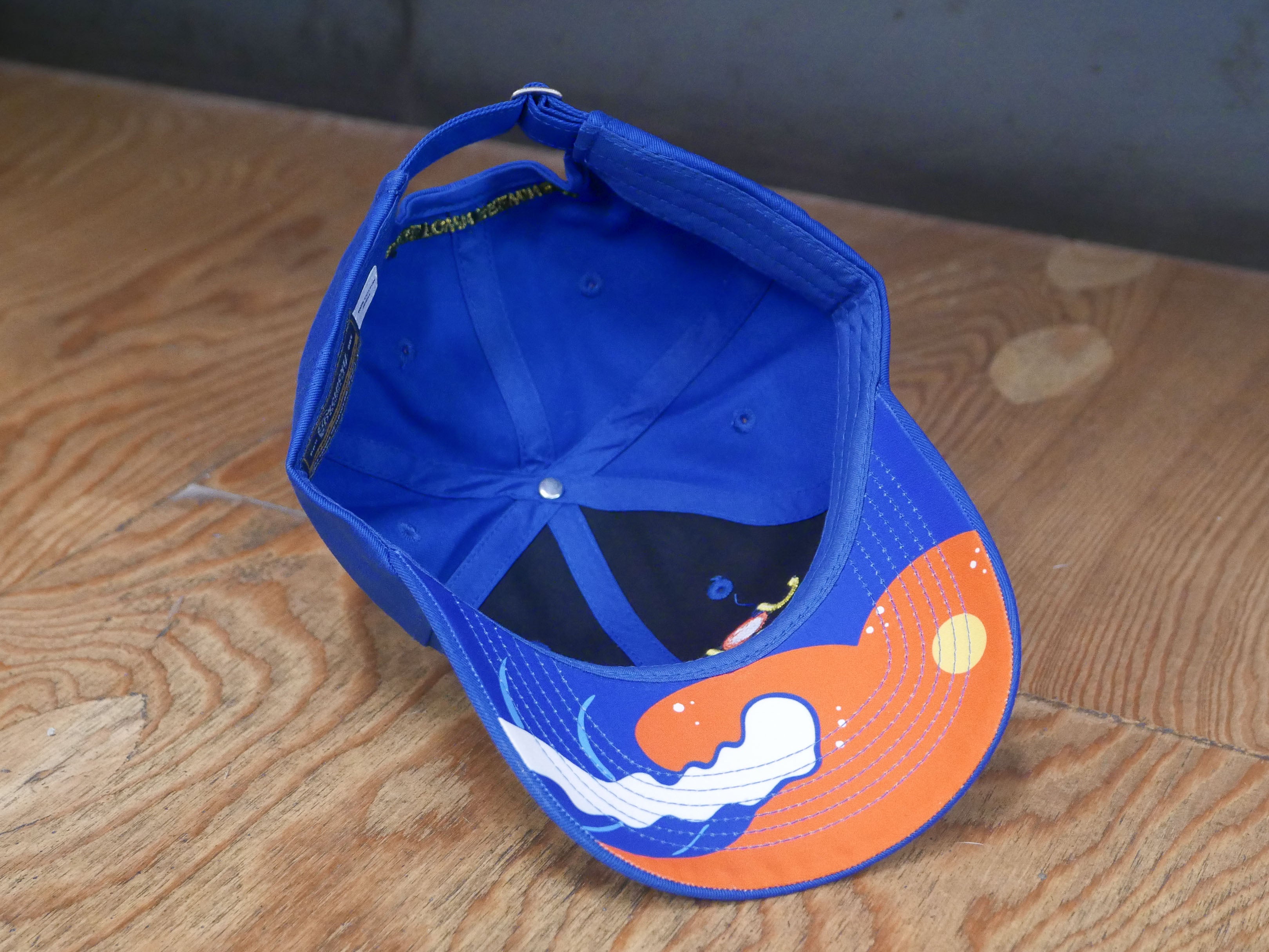 the underside of the same hat with a wave and sun design in orange, yellow, white and blue. 